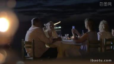 在海边的家庭晚餐中，年轻女子用手机拍摄年迈的父母，离焦的海滩火炬正在燃烧